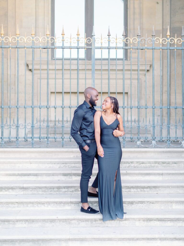 couple stand and look each other on the stair of the courtside of the louvres museum during Engagement session Louvres Paris