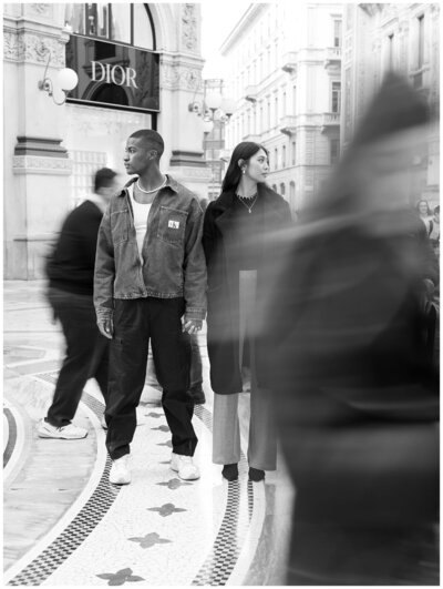 Un couple marche dans la Galleria à Milan, veste en jean et manteau long.